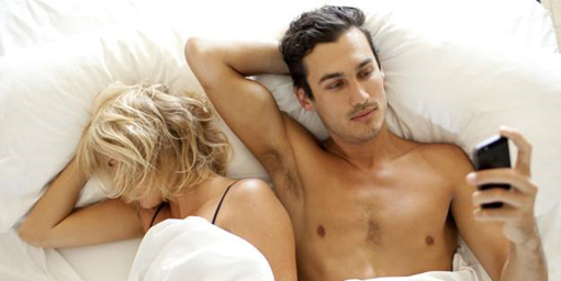 couple in bed man looking at phone shirtless